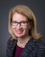 Headshot of Cheryl Druehl, a woman smiling wearing glasses and a textured blazer