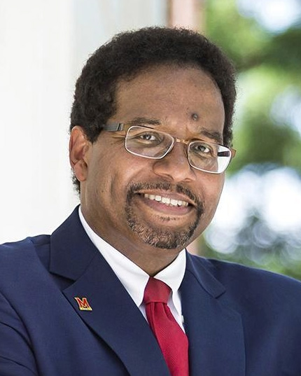 Headshot of Darryll Pines, a man smiling wearing glasses, a dark suit, and a red tie