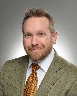 Headshot of Eric Moret, a smiling man wearing a green suit