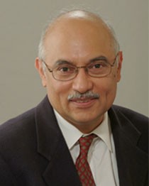 Headshot of P.R. Kumar, a man smiling wearing glasses, a dark suit, and a red tie