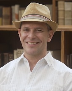 Headshot of Patrick Shafto, a man smiling wearing a hat and button down shirt
