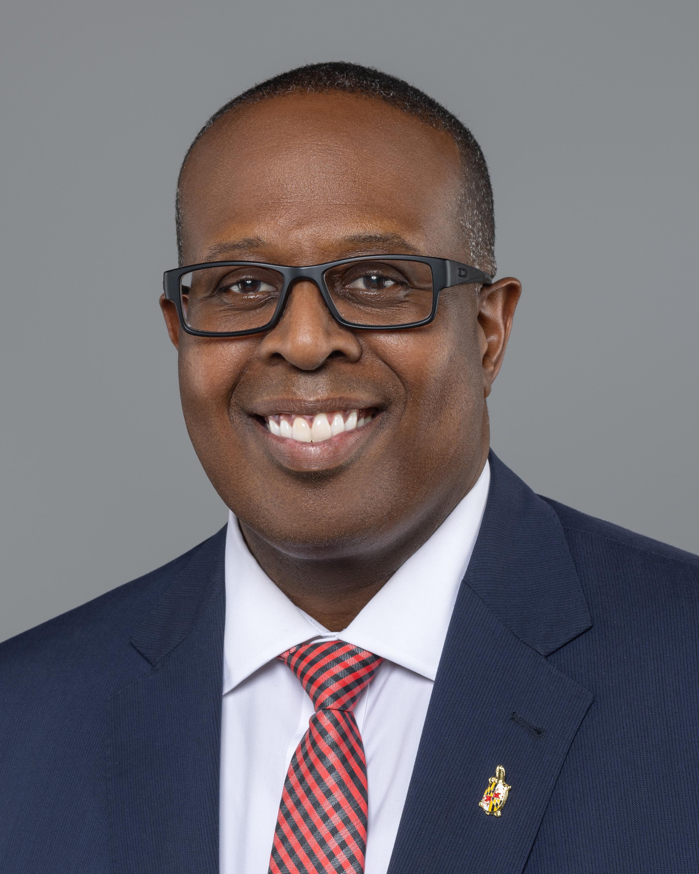 Headshot of Sam Graham, a man smiling wearing glasses and a suit