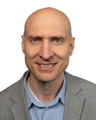 Headshot of Srdjan Lukic, a man smiling wearing a polo shirt and blazer