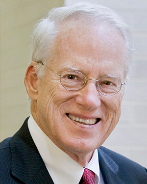 Headshot of William Kirwan, a man smiling wearing glasses and a suit